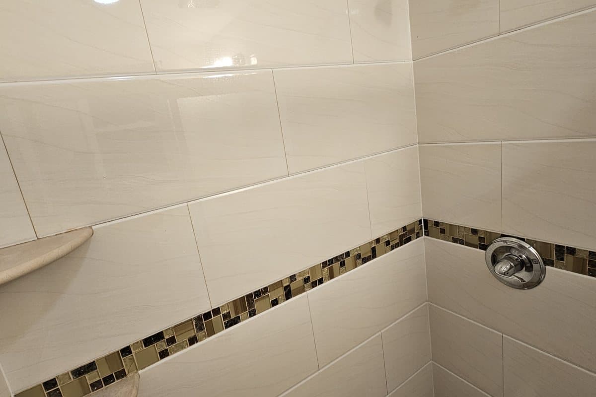 Freshly cleaned white-tiled shower with a glass-tile accent border